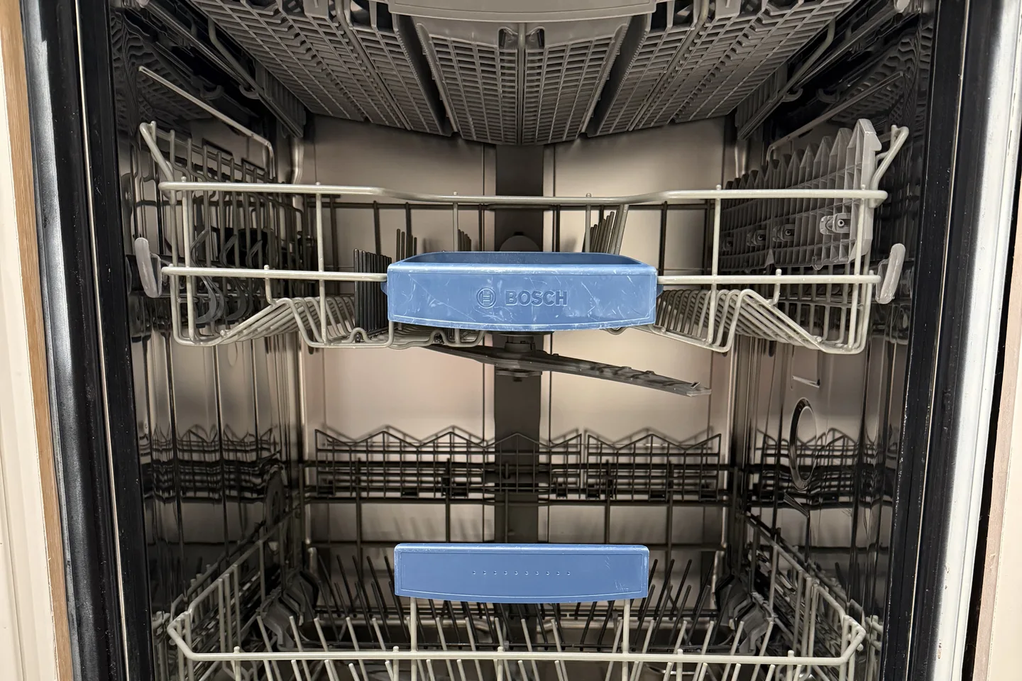 Открытая посудомойка Bosch с пустыми корзинами и синими ручками.